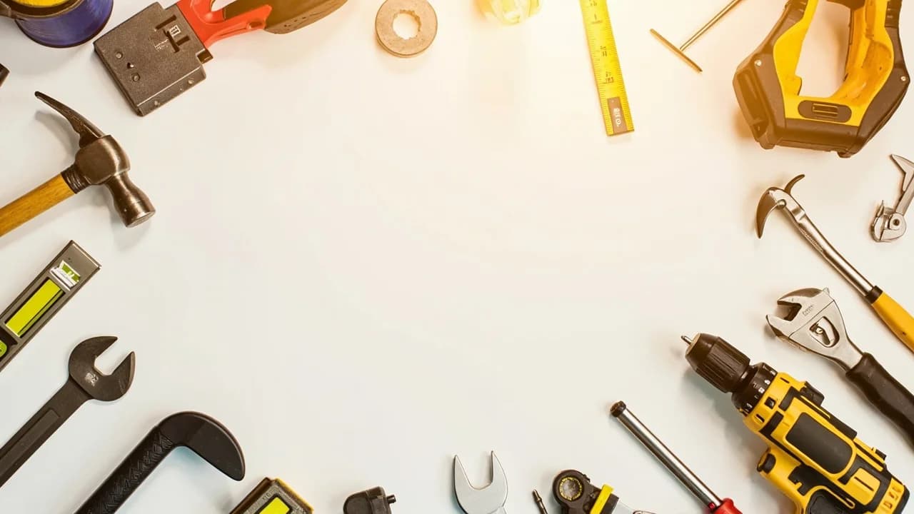 Neatly arranged home renovation tools including hammer, drill, tape measure, level and screwdrivers on clean white surface with warm golden lighting, no people